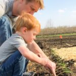 Two children transplanting onion seedlings into garden soil.