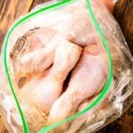 Raw chicken drumsticks in a resealable bag with olive oil, preparing for seasoning.