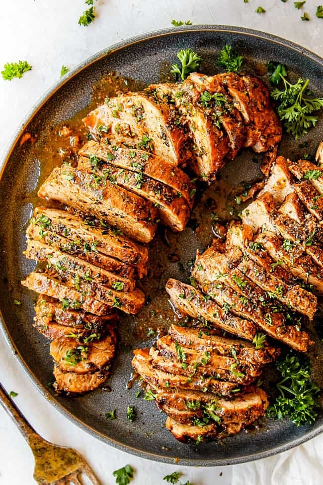 Close-up of juicy baked pork tenderloin slices on a cutting board, ready to serve.