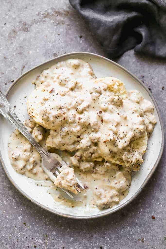 Biscuits and gravy on a plate with a bite taken out by a fork.