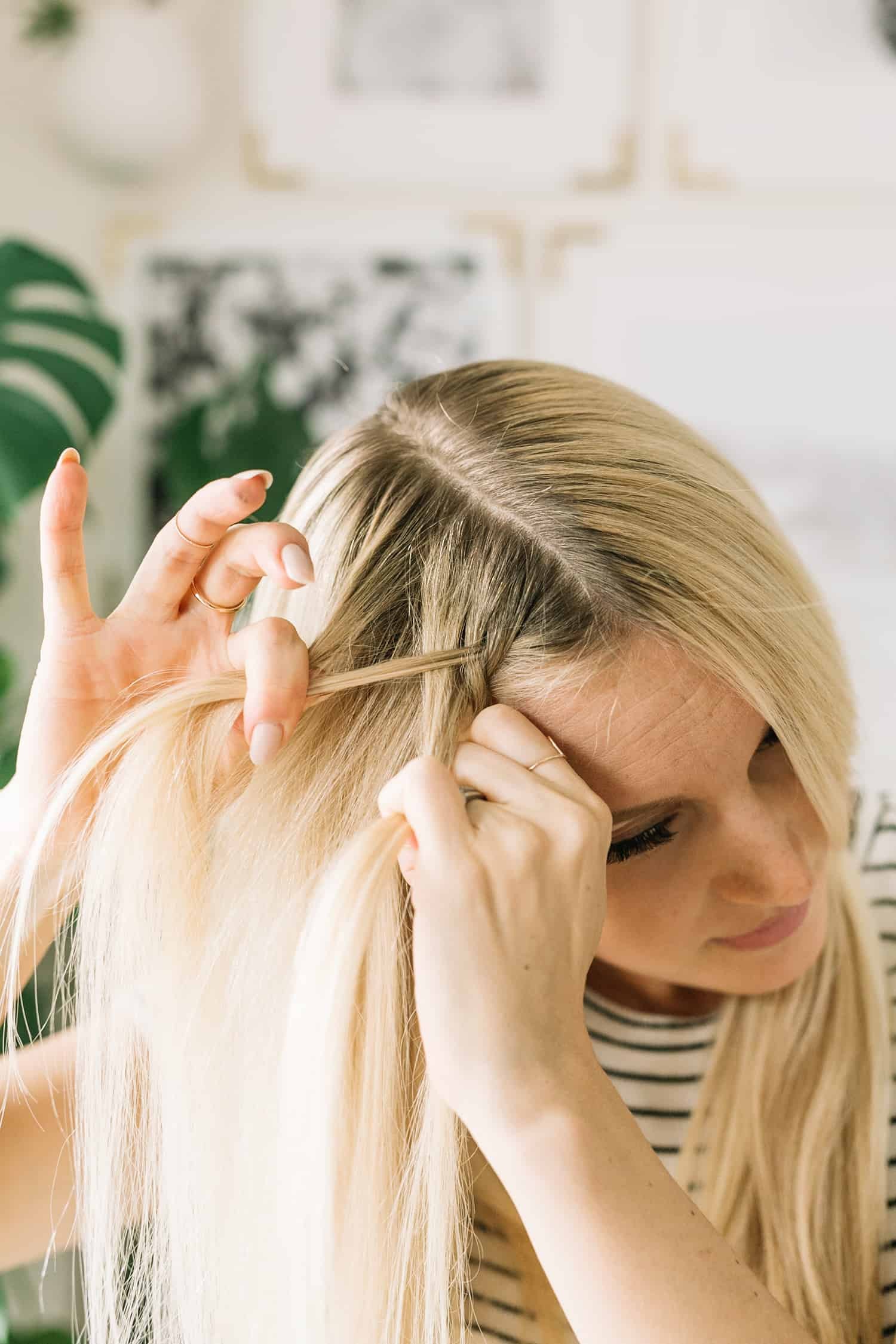 Woman preparing to dutch braid her hair, parting hair with hair extension clipped in, demonstrating initial setup for braid with extensions