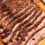 Close-up of sliced beef brisket on a wooden cutting board, showcasing its juicy and tender texture.