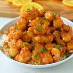 Close-up of homemade Orange Chicken featuring crispy chicken and a vibrant orange sauce, garnished with orange zest and green onions.