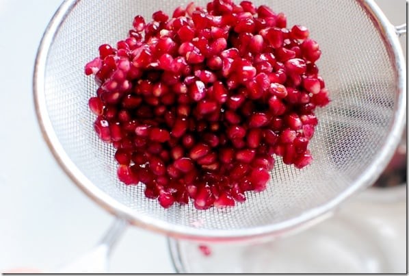 Close-up of a hand holding a halved pomegranate, showcasing the ruby-red arils inside.