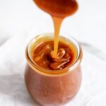 Close-up of golden homemade caramel sauce dripping from a spoon into a glass jar