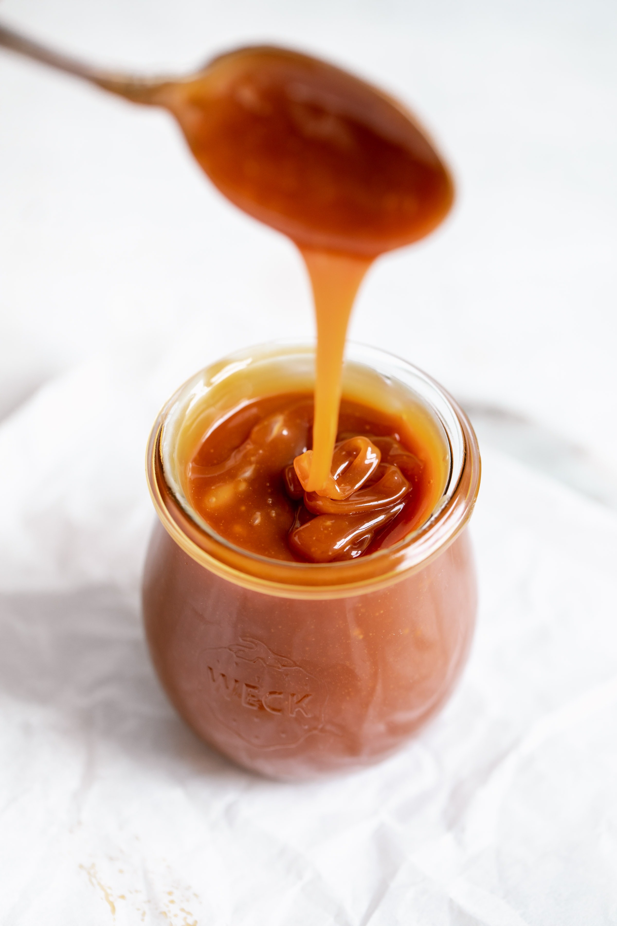 Close-up of golden homemade caramel sauce dripping from a spoon into a glass jar