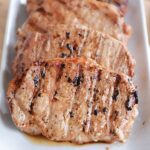 Four cooked, grilled pork chops lined up on a plate.