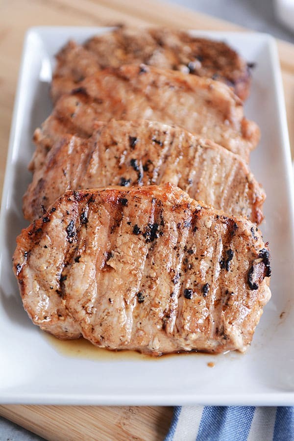 Four cooked, grilled pork chops lined up on a plate.