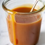 close up of caramel sauce in glass jar with spoon, running down side