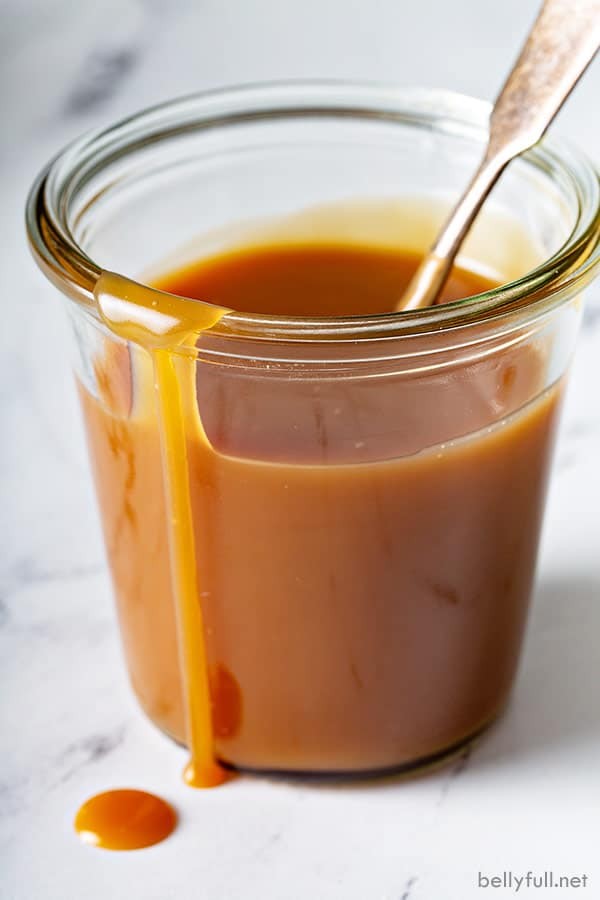 close up of caramel sauce in glass jar with spoon, running down side