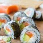 Variety of homemade sushi rolls beautifully arranged on a dark wooden serving board, showcasing different fillings and textures.