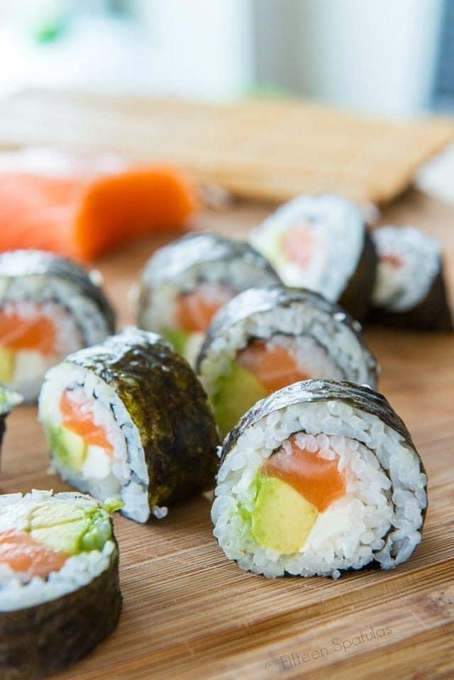 Variety of homemade sushi rolls beautifully arranged on a dark wooden serving board, showcasing different fillings and textures.