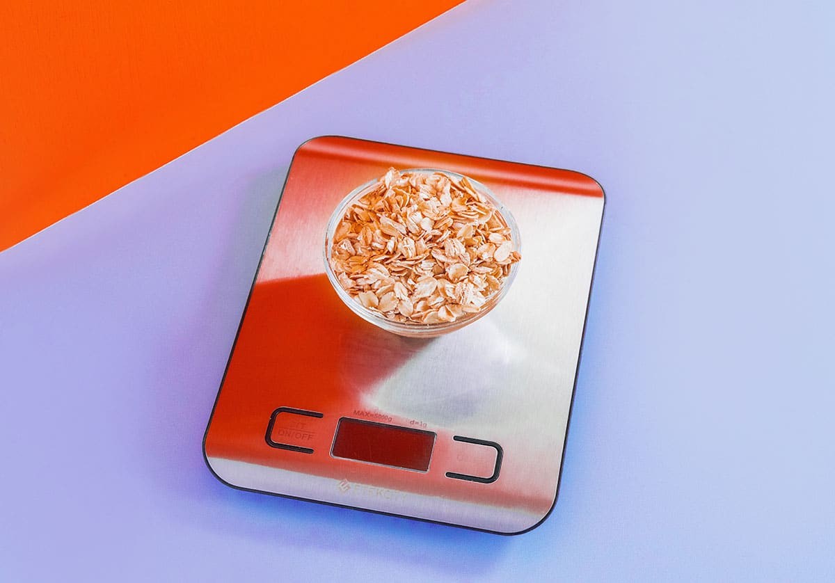 Close-up of oatmeal being weighed in grams on a digital kitchen scale, emphasizing precise measurement for cooking and baking.