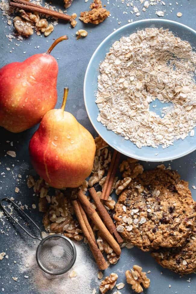 A small blue bowl filled with raw oatmeal next to cinnamon sticks, pears and walnuts, illustrating kitchen measurements for a recipe.