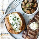 A plate with a baked potato topped with sour cream, a steak topped with butter, and a bowl of balsamic mushrooms on a plate.