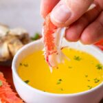 A close-up shot showcasing a hand dipping a succulent piece of crab meat into a bowl of melted butter, emphasizing the tender texture and inviting flavor.