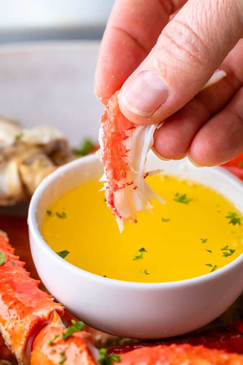 A close-up shot showcasing a hand dipping a succulent piece of crab meat into a bowl of melted butter, emphasizing the tender texture and inviting flavor.