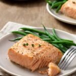 Cooked salmon fillet on white plate with green beans.