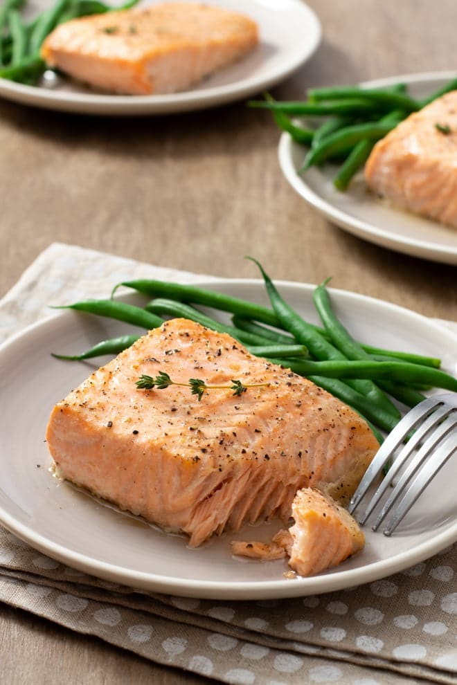 Cooked salmon fillet on white plate with green beans.