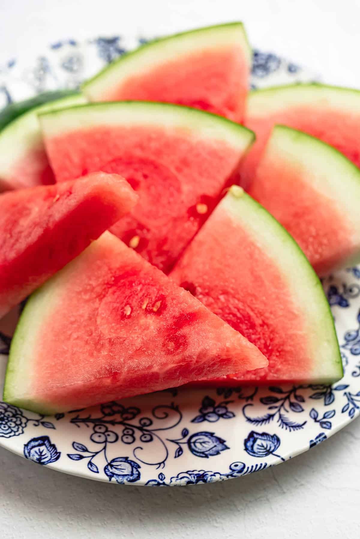 Close up vibrant watermelon wedges on a blue and white plate, showcasing juicy red flesh.