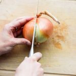 Close-up of a knife cutting into a yellow onion on a wooden cutting board