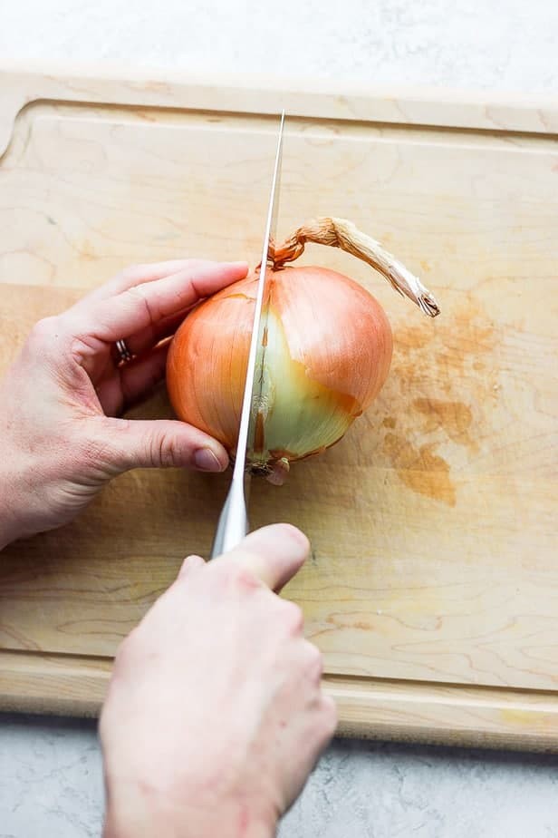 Close-up of a knife cutting into a yellow onion on a wooden cutting board