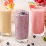 three different smoothies in glasses with a variety of fruit in the background