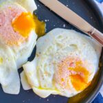 Over easy eggs on blue plate with knife in background.