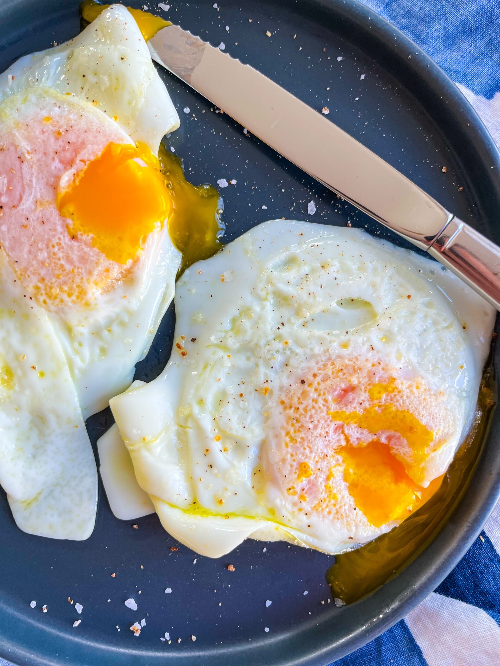 Over easy eggs on blue plate with knife in background.