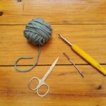 Essential crochet tools for beginners: yarn, crochet hook, darning needle, and scissors.