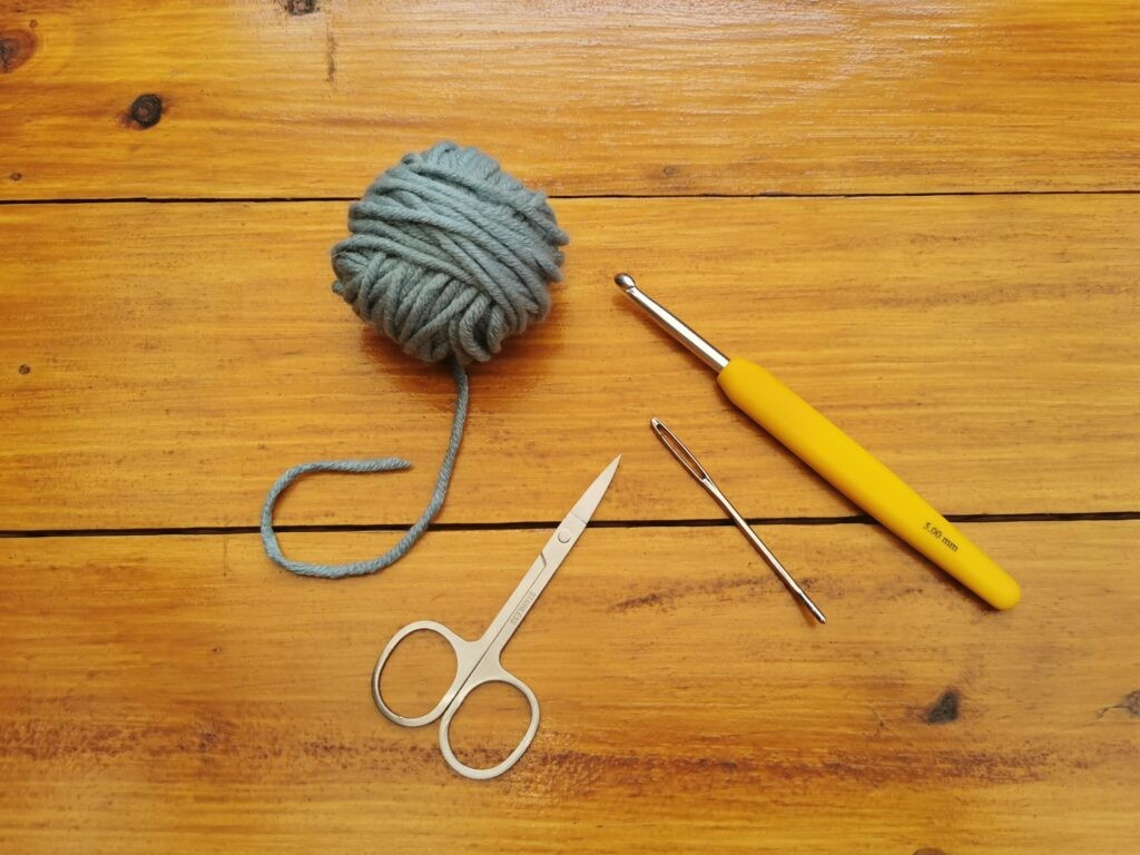 Essential crochet tools for beginners: yarn, crochet hook, darning needle, and scissors.