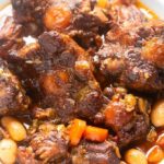 jamaican oxtail in a white bowl with blue napkin in background