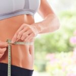 Woman measuring her waist with a tape measure, illustrating methods to reduce belly fat in one week.