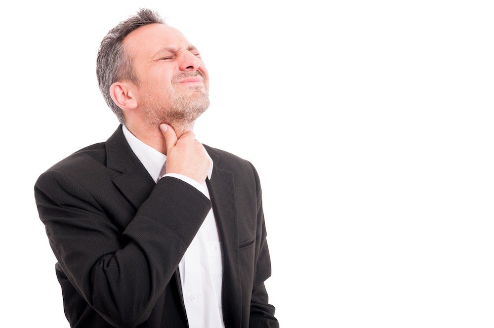 Man looking at his throat in a mirror, indicating potential tonsil stones and related symptoms like bad breath and sore throat