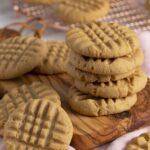 A tempting stack of homemade peanut butter cookies on a rustic wooden board, showcasing their classic criss-cross pattern and golden-brown edges.