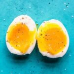 A perfectly soft boiled egg, halved to reveal a runny yolk, against a vibrant blue backdrop.