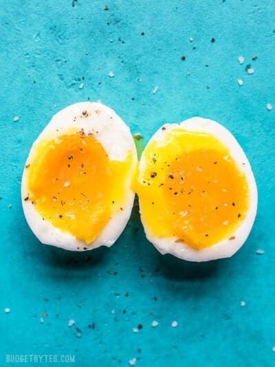 A perfectly soft boiled egg, halved to reveal a runny yolk, against a vibrant blue backdrop.