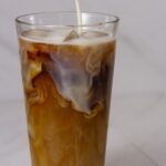 pouring frothed milk onto an ice coffee drink.