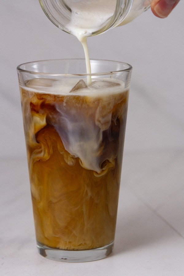 pouring frothed milk onto an ice coffee drink.