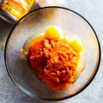 Ingredients for pumpkin pie batter in mixing bowls, showcasing pumpkin puree, eggs, sugar, and spices.