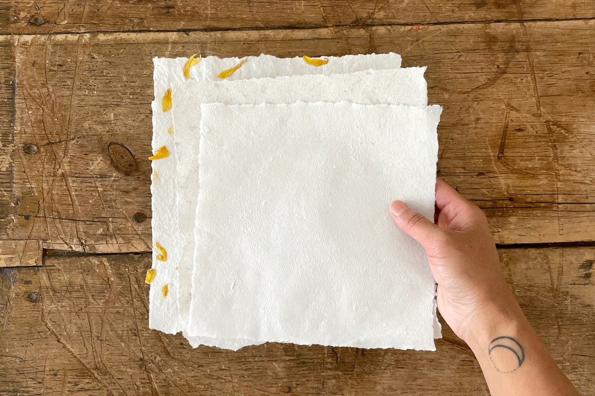 Hands holding a piece of freshly made recycled paper, showcasing its texture and handmade quality.