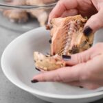 Hands removing bones from canned salmon in a bowl, demonstrating preparation for homemade salmon patties recipe.