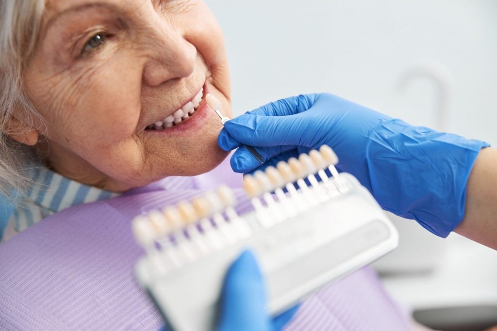 Gloved left hand of dentist holding implant tray and right hand holding implant to woman's mouth, illustrating implant-supported dentures procedure