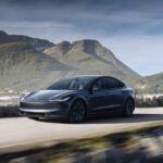 A grey Tesla Model 3 driving down a waterside highway