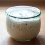 A jar of active sourdough starter showing bubbles and rise.