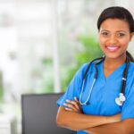 Smiling nurse practitioner in blue scrubs with arms folded, representing the rewarding career and competitive salary of nurse practitioners.