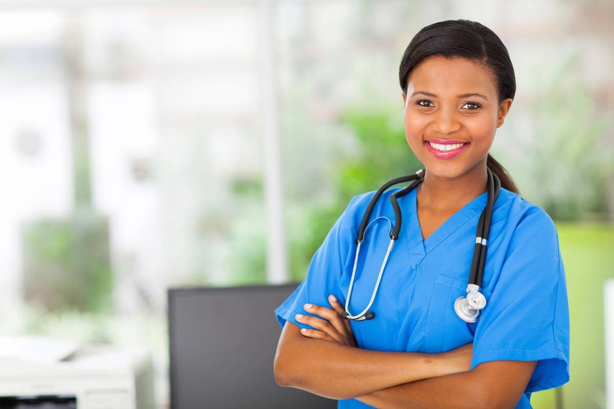 Smiling nurse practitioner in blue scrubs with arms folded, representing the rewarding career and competitive salary of nurse practitioners.