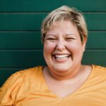 Portrait of a woman smiling outdoors with green background.