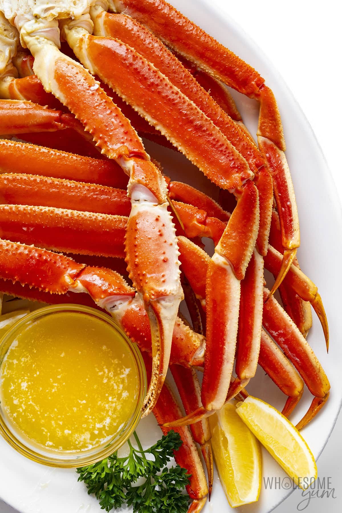 Crab legs on a platter with melted butter and lemon wedges.