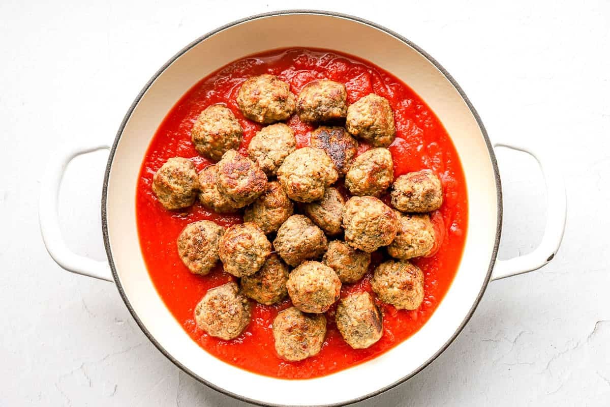 Cooked meatballs in marinara sauce after being pan fried.